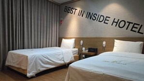Une chambre d’hôtel avec deux lits, une enseigne fixée au mur indiquant « MEILLEUR HÔTEL », et un plancher en bois.