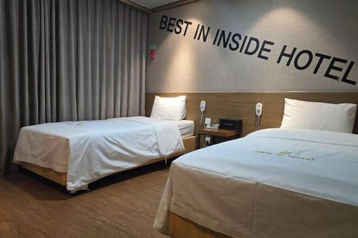 A hotel room with two beds, a wall-mounted sign reading 'BEST IN INSIDE HOTEL,' and a wooden floor.