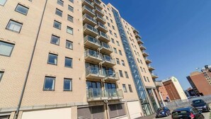 A multi-story residential building with balconies, a brick facade, and a clear blue sky.
