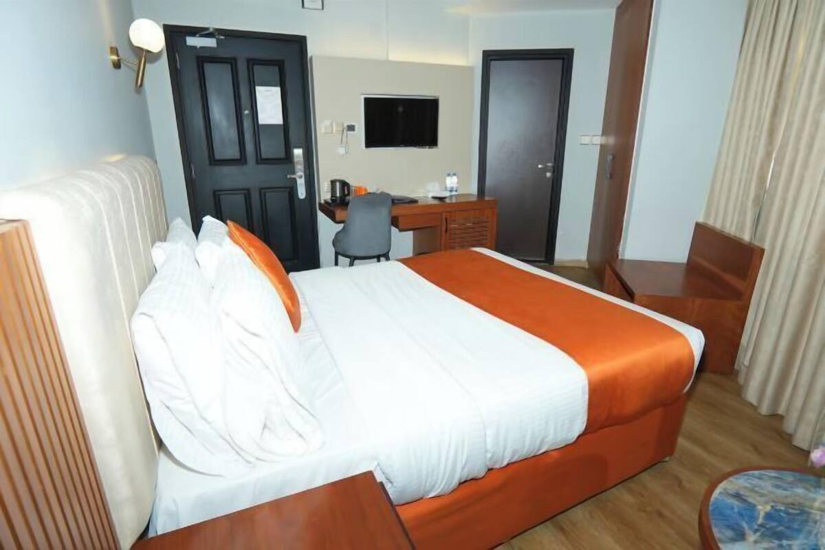 A hotel room with a bed, a desk, a chair, a television, and a door.