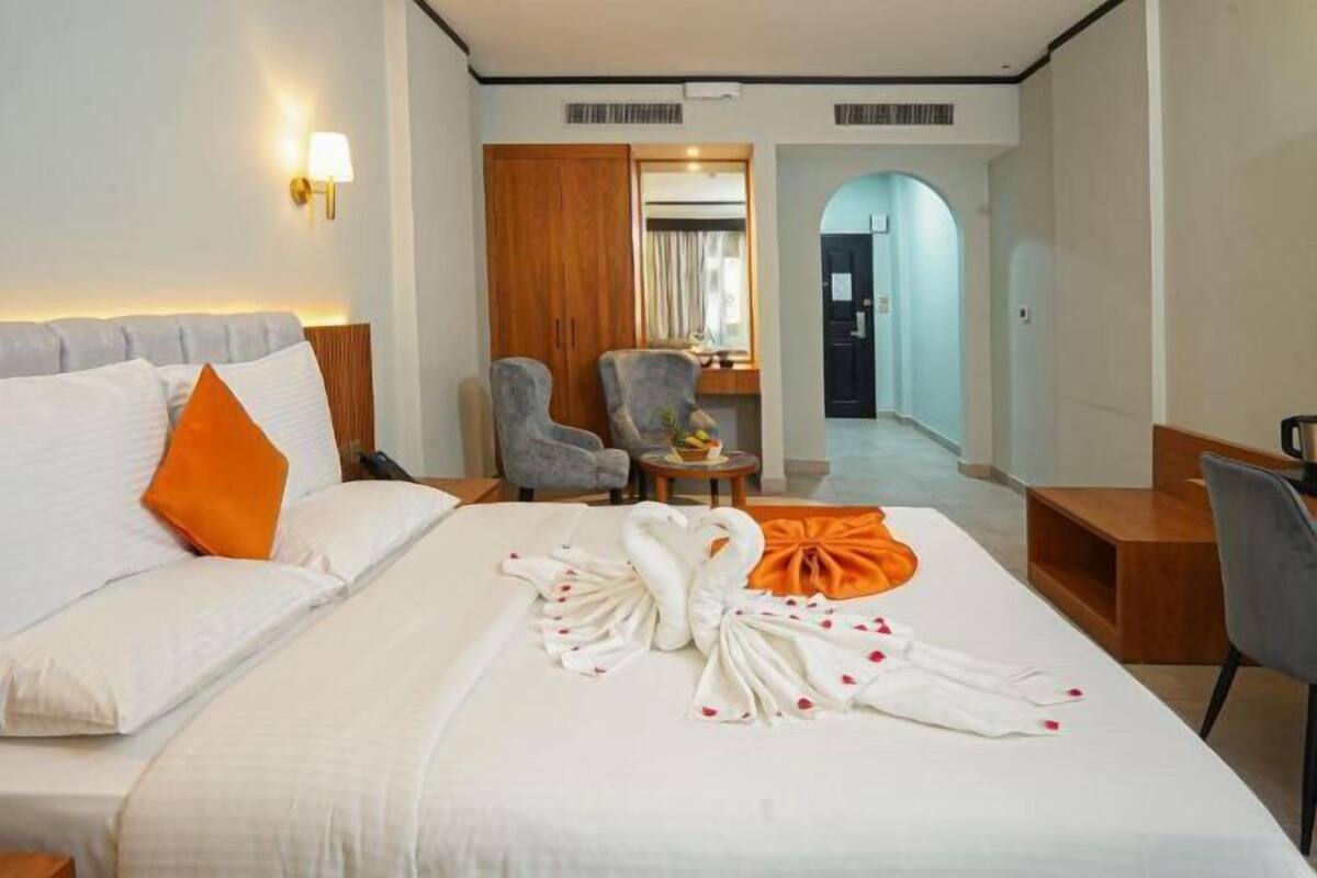 A hotel room with a bed, a desk, a chair, a wardrobe, and a bathroom visible through an archway.