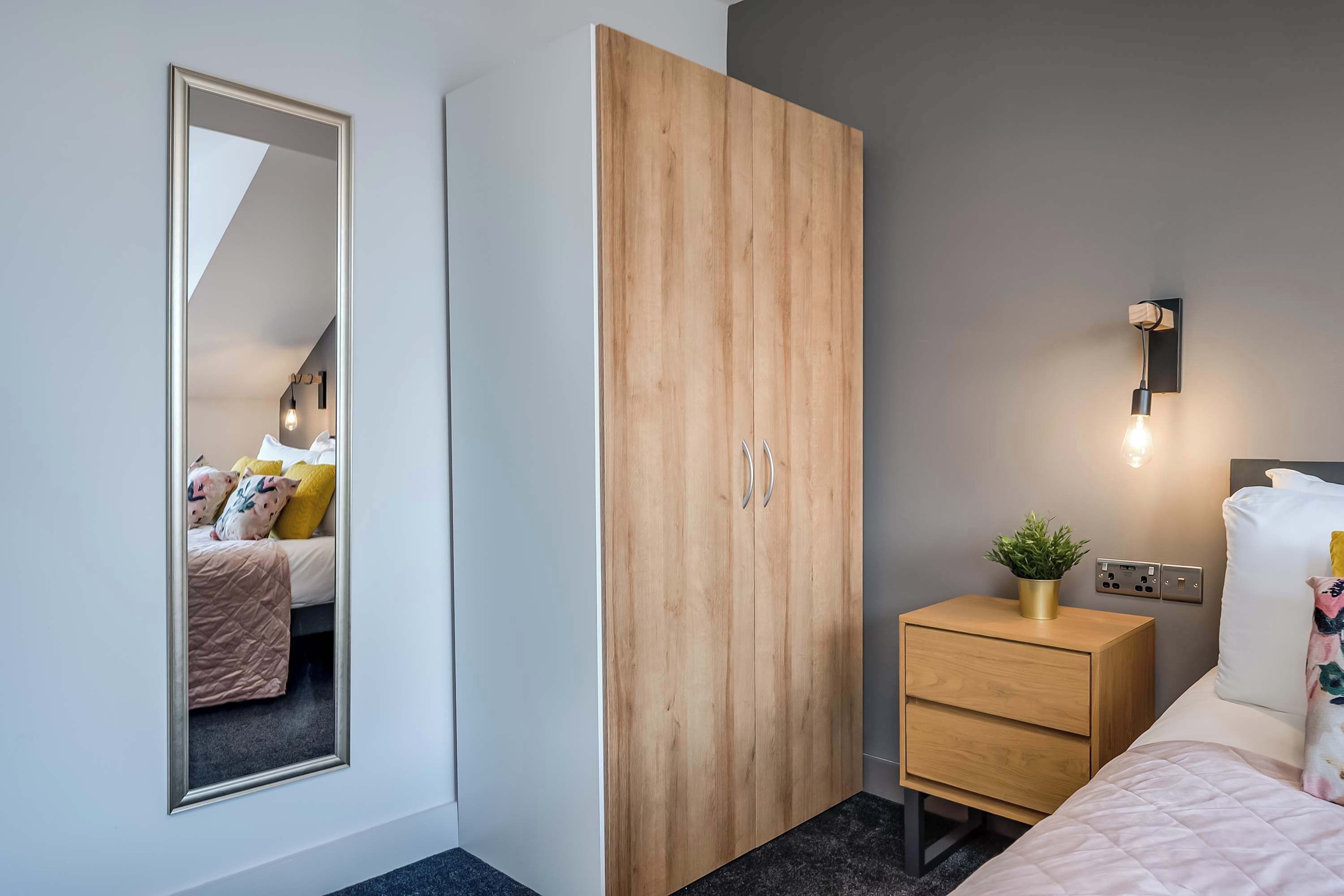 Ein Schlafzimmer mit großem Kleiderschrank, einem Nachttisch mit Pflanze und einem Spiegel an der Wand.