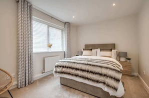 Quarto com uma cama, mesa de cabeceira, abajur, cadeira e janela com cortinas.