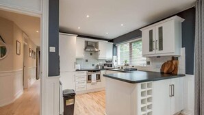 A modern kitchen with white cabinetry, a central island, and a window with blinds. - Windsor | 2-Bed + Free Parking | Lisburn Road (Belfast)