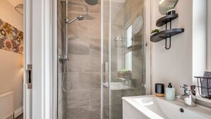 A modern bathroom with a glass-enclosed shower, a white sink with a mirror, and a small shelf with toiletries.