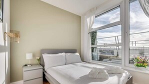 Una camera da letto moderna con una grande finestra, un comodino con una lampada e un letto rifatto con cura.