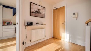 Una cucina moderna con mobili bianchi, pavimento in legno, un quadro appeso e un cartello con la password del Wi-Fi.