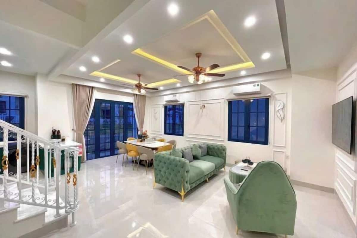 A modern living room with a green sofa, a dining area, and a staircase.