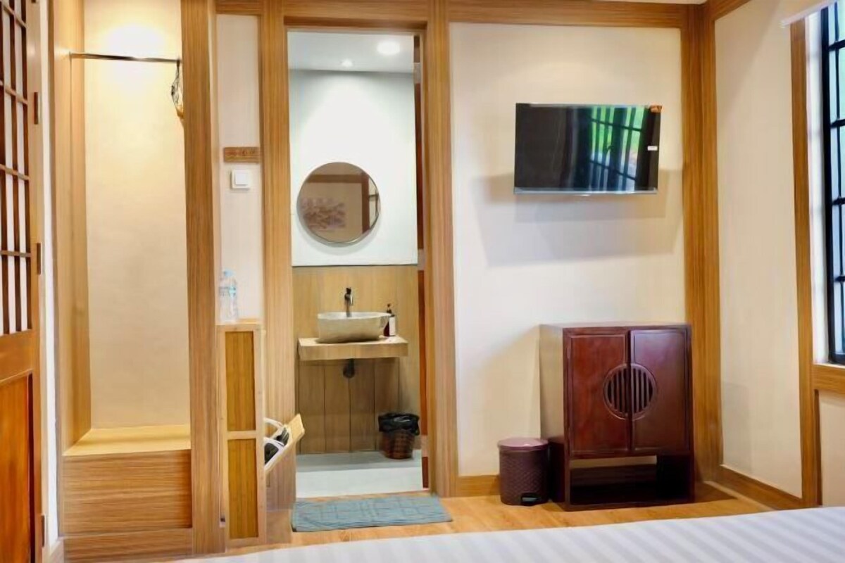 A room with a wooden floor, a bed, a TV mounted on the wall, a sink, and a cabinet.