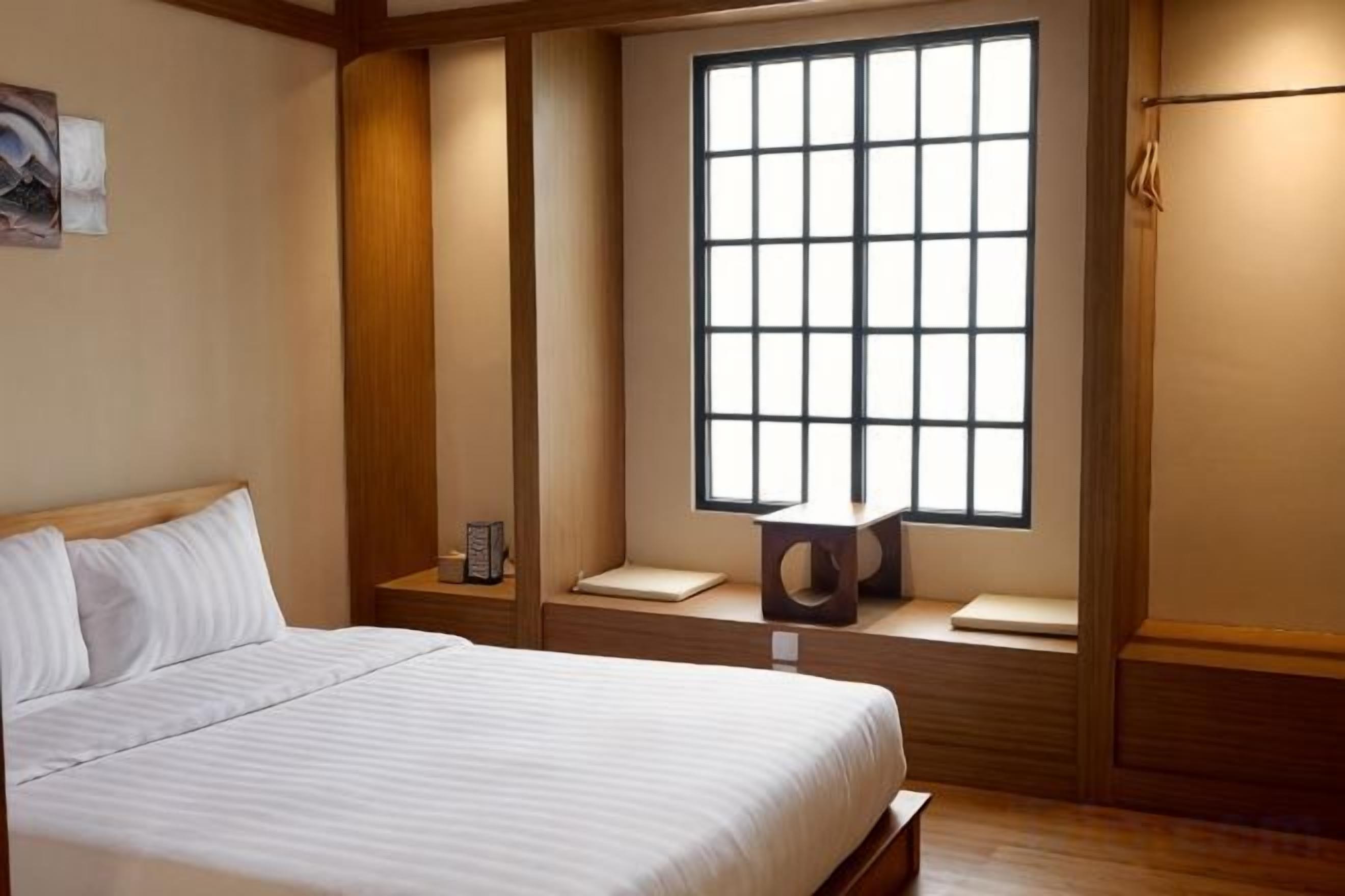 Habitación de hotel con cama, ventana con vistas, mesita de noche y tocador.