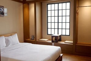 Een hotelkamer met een groot raam, een bed, een nachtkastje en een klein krukje.