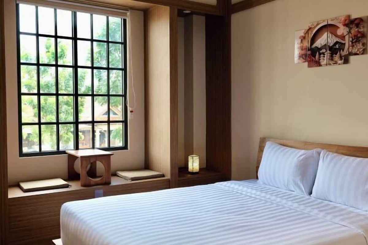 Quarto de hotel com uma janela grande, uma cama, uma mesinha de cabeceira e uma obra de arte na parede.