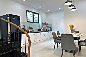 A modern kitchen with white cabinets, a dining area with a round table and chairs, and a staircase with a black railing.