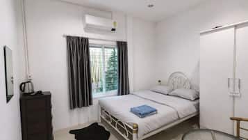 A bedroom with a bed, a dresser, a window with curtains, an air conditioning unit, and a chair.