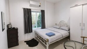 A bedroom with a bed, a dresser, a window with curtains, an air conditioning unit, and a small table. - Your House kkn. (Khon Kaen)