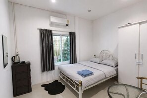 Un dormitorio con cama, cómoda, ventana con cortinas, equipo de aire acondicionado y una pequeña mesa.