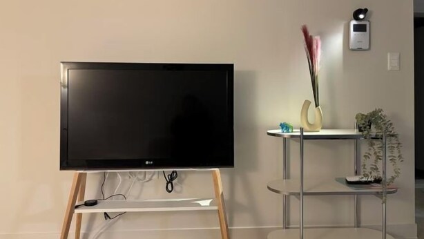 A flat-screen TV on a wooden stand, a small table with decorative items, and a wall-mounted thermostat. - Aurora Gyeongju (Gyeongju)
