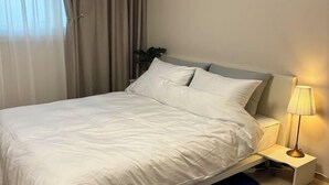 A bed with white linens, a bedside table with a lamp, and a plant in the corner. - Aurora Gyeongju (Gyeongju)