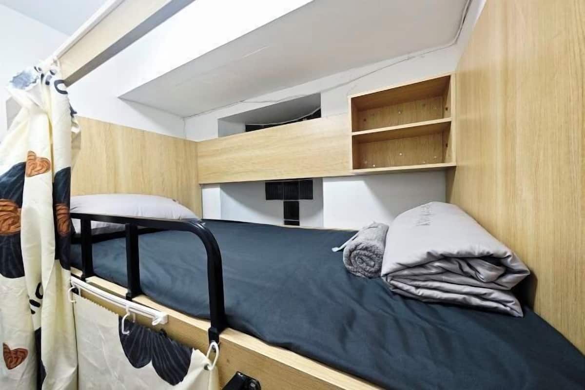 A bunk bed with a headboard, a small shelf above, and a curtain with a pattern.