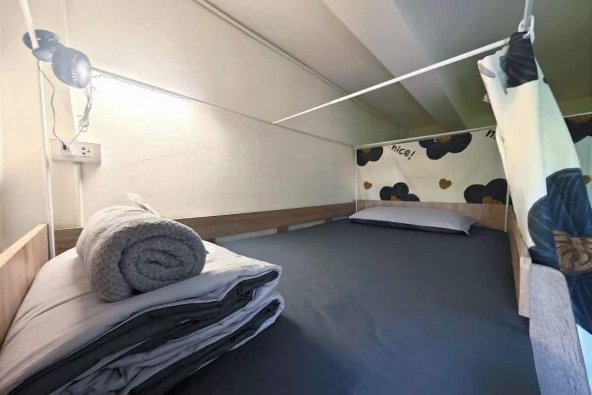 A single bed with a headboard, a wall-mounted lamp, and a curtain with a heart pattern.