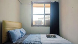 Una habitación pequeña con cama individual, ventana, cabecera y ropa de cama con manta y almohadas azules.