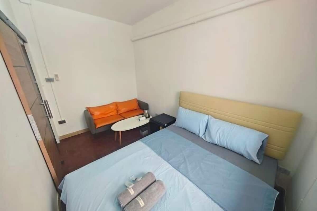 A hotel room with a bed, a small table, an orange sofa, and a door.
