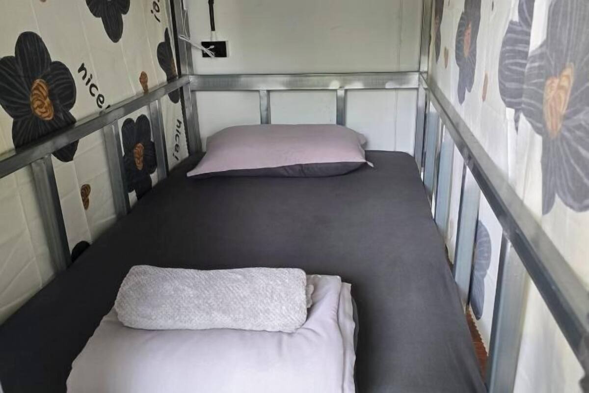 A single bed with a metal headboard and a pillow, in a room with floral wallpaper.