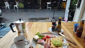 Una mesa de desayuno con una taza de café, un plato de huevos, tostadas y jamón, además de salsas y acompañamientos.