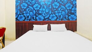 Habitación de hotel con cama, dos almohadas, cabecero de madera y pared con estampado floral.