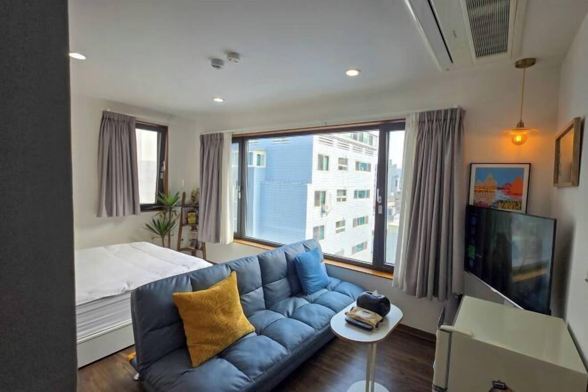 A modern hotel room with a bed, sofa, TV, and large windows.