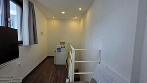 Un pasillo estrecho con una cama, un televisor y un refrigerador.