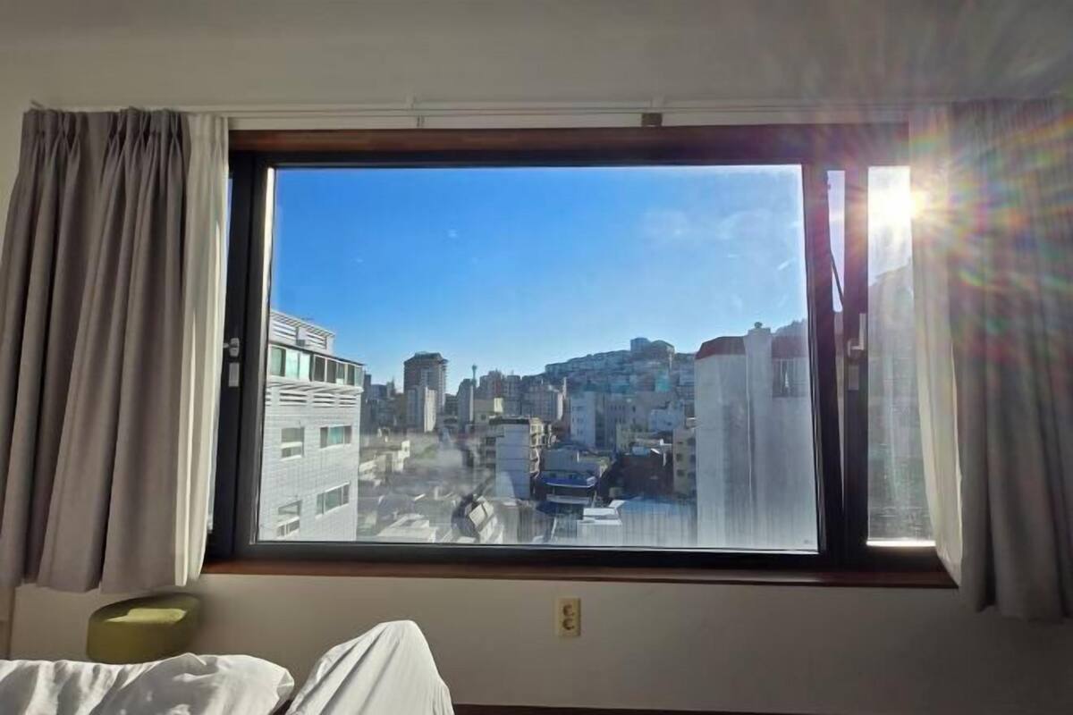 A hotel room with a large window offering a city view.