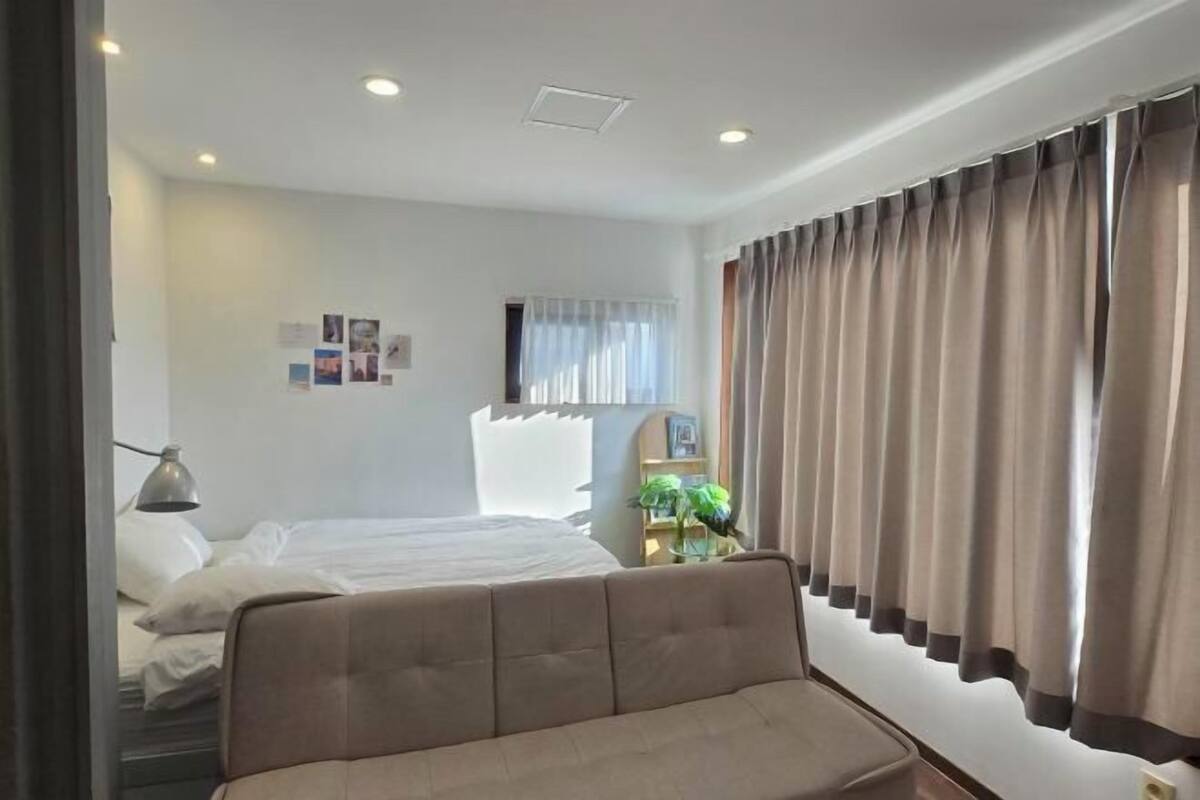 A hotel room with a bed, a sofa, a desk, a lamp, a window with curtains, and a wall with pictures.