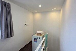A narrow hallway with a white wall, a grey curtain, and a small refrigerator with a basket on top.