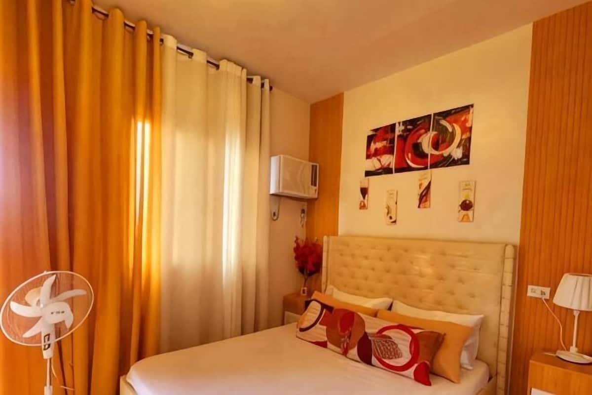 Una habitación de hotel con cama, cortinas, ventilador, aire acondicionado y obras de arte.