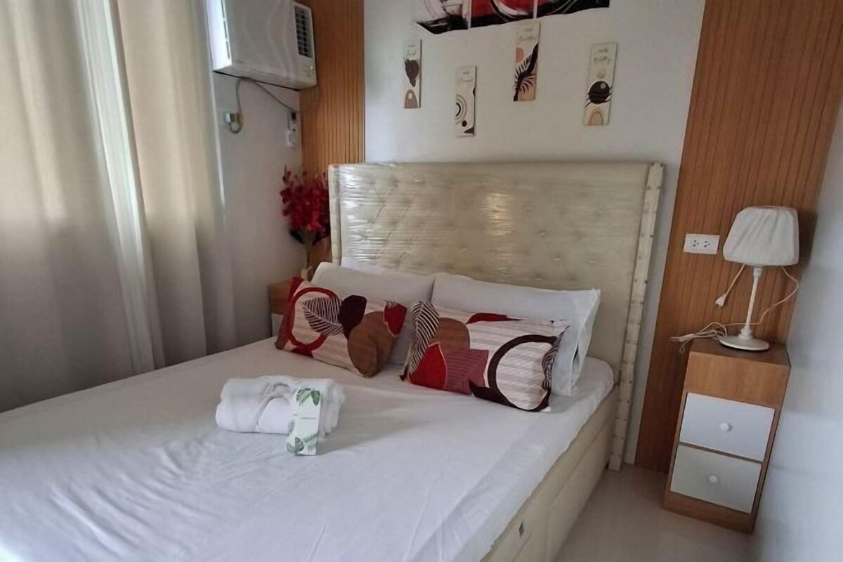 A neatly made bed with pillows and a folded towel, a bedside lamp, and a wall-mounted air conditioner.