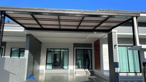 A modern building with a covered entrance, large windows, and a visible blue cleaning tool. - Poome House By Zuzu (Hat Yai)