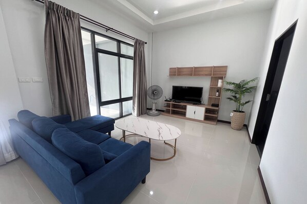 A living room with a blue sofa, a white marble coffee table, a TV, and a fan.