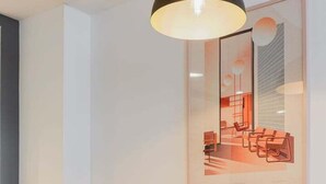 Eine moderne Küche mit Barbereich, ausgestattet mit einer Pendelleuchte, gelben Sitzhüllen an den Stühlen und einem gerahmten Architekturprint an der Wand.