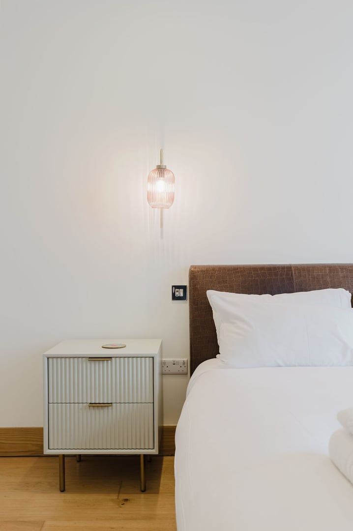A bedroom with a bed, a nightstand, and a wall-mounted light fixture.