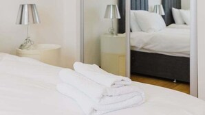 Ein Hotelzimmer mit großem Spiegel, einem Bett mit weißer Bettwäsche, zwei Nachttischlampen und einem Kleiderschrank.