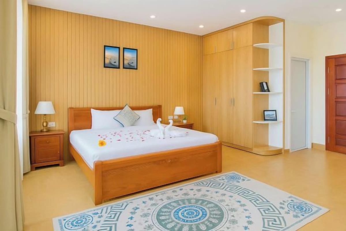 Un dormitorio con cama de madera, mesitas de noche, armario y alfombra estampada.