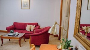 Una sala de estar con un sofá rojo, una mesa de centro de madera, una lámpara y una mesa de comedor con una planta.