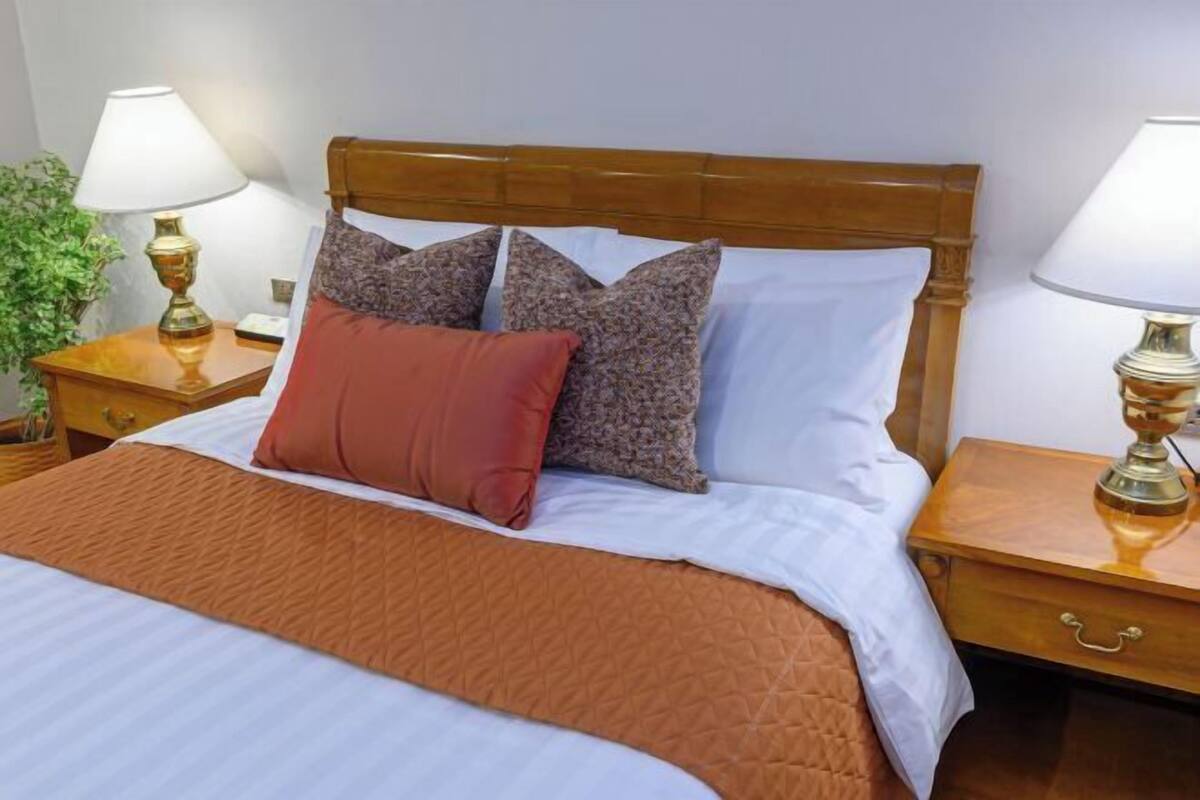 A hotel room with a large bed, two bedside lamps, a wooden headboard, and a nightstand with a drawer.