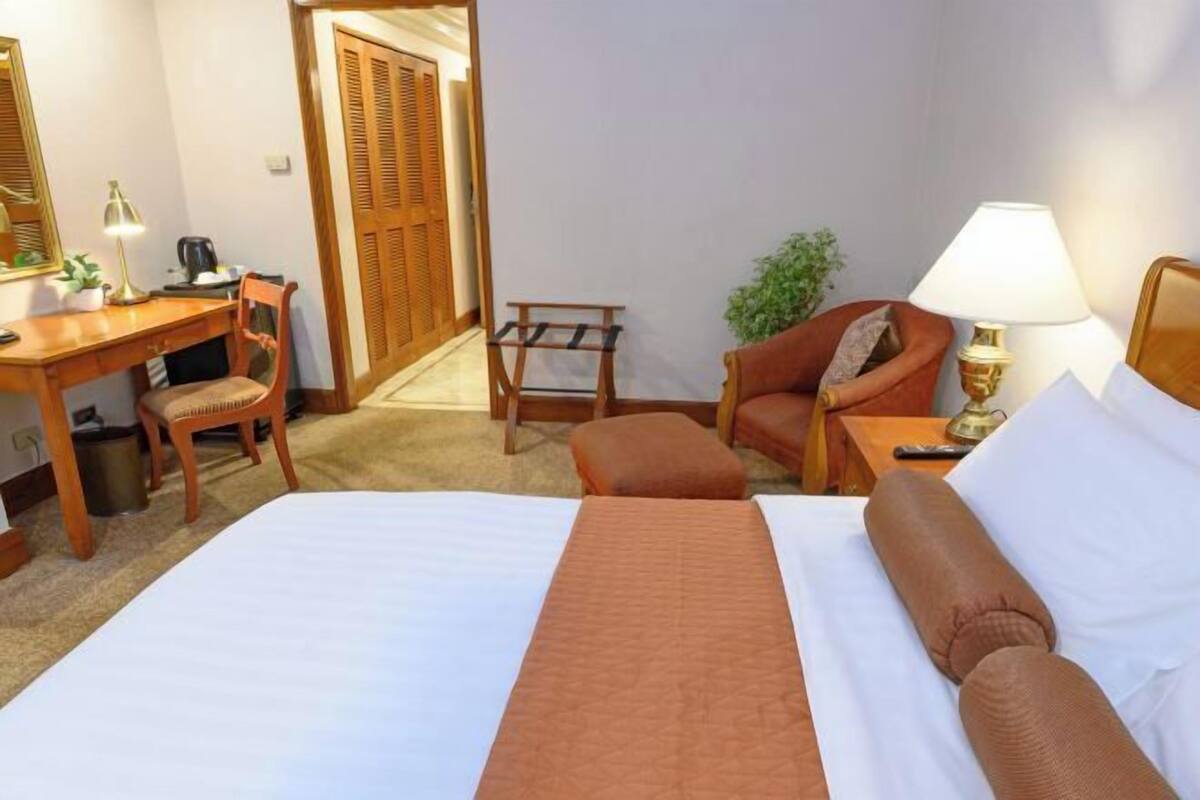 A hotel room with a bed, a desk, a chair, a lamp, and a small table.