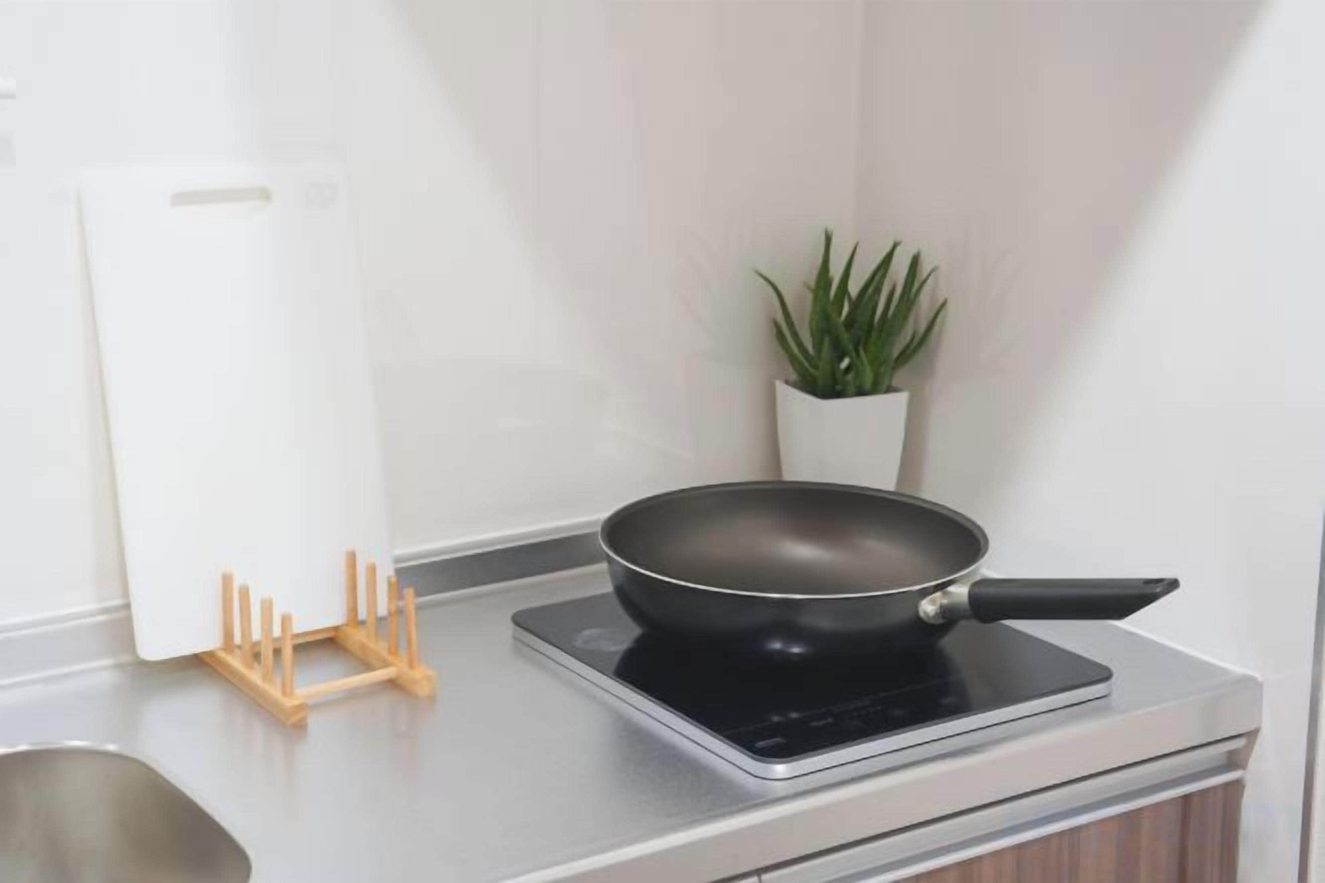 A kitchen with a stove, a frying pan, a cutting board, and a potted plant.