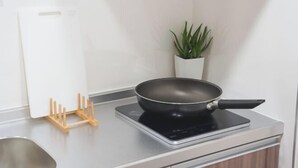 A kitchen with a black frying pan on an induction cooktop, a white cabinet, and a potted plant. - Blessed Residence 505 (Osaka)