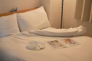Un lit bien fait, avec du linge de lit blanc, un bol et une cuillère sur une assiette, et un magazine posé sur le lit.
