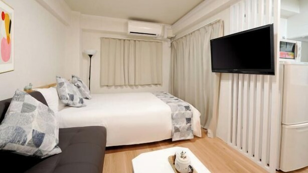 A hotel room with a bed, a sofa, a flat-screen TV, an air conditioning unit, and a refrigerator. - Blessed Residence 505 (Osaka)