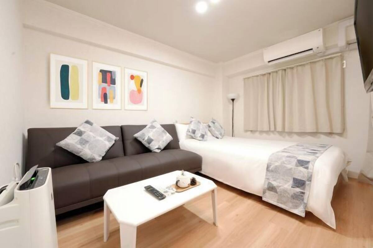 A modern hotel room with a sofa, a bed with a patterned blanket, a small table with a remote control, and artwork on the wall.